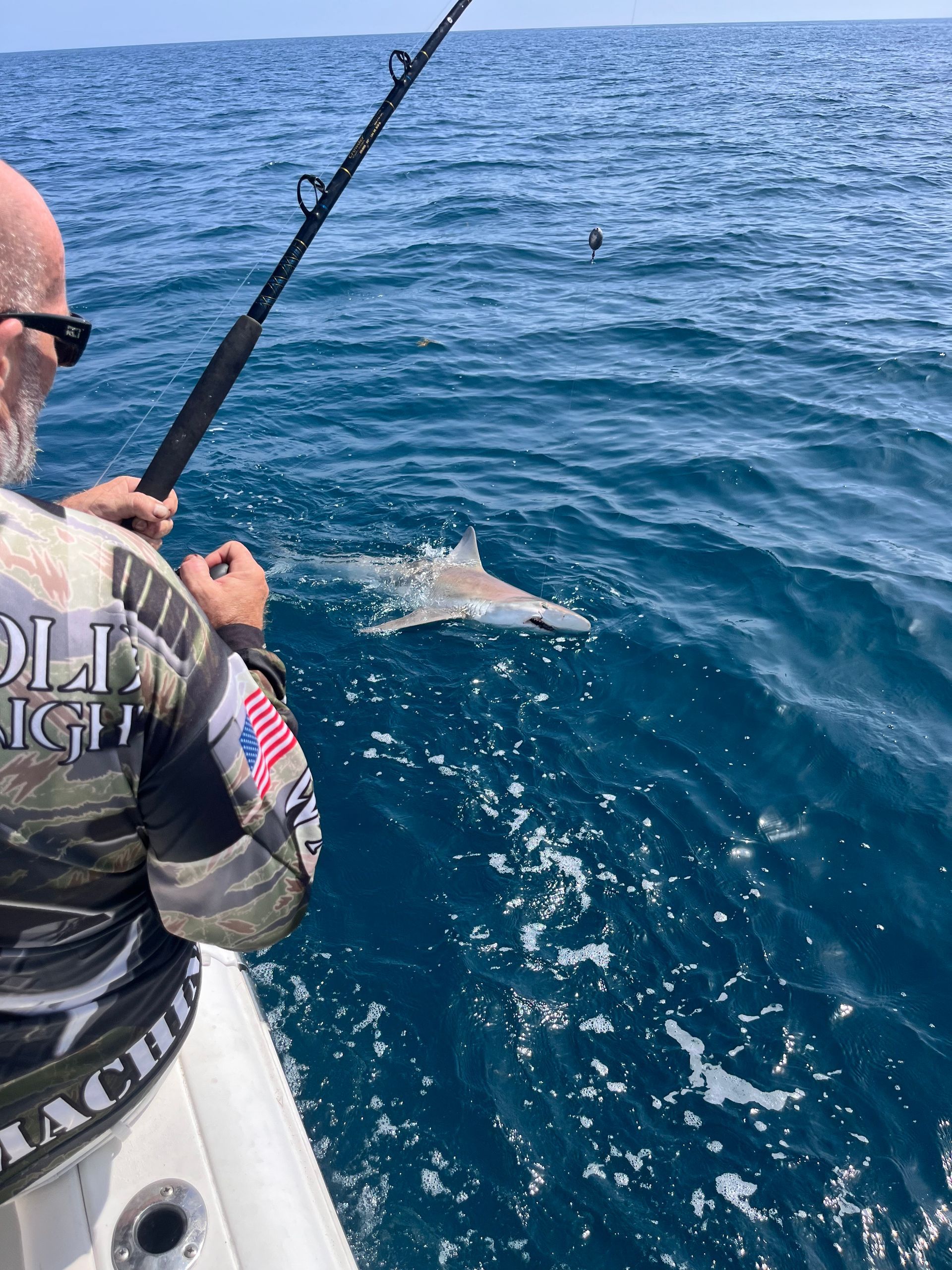 A man is fishing in the ocean with a shark in the background