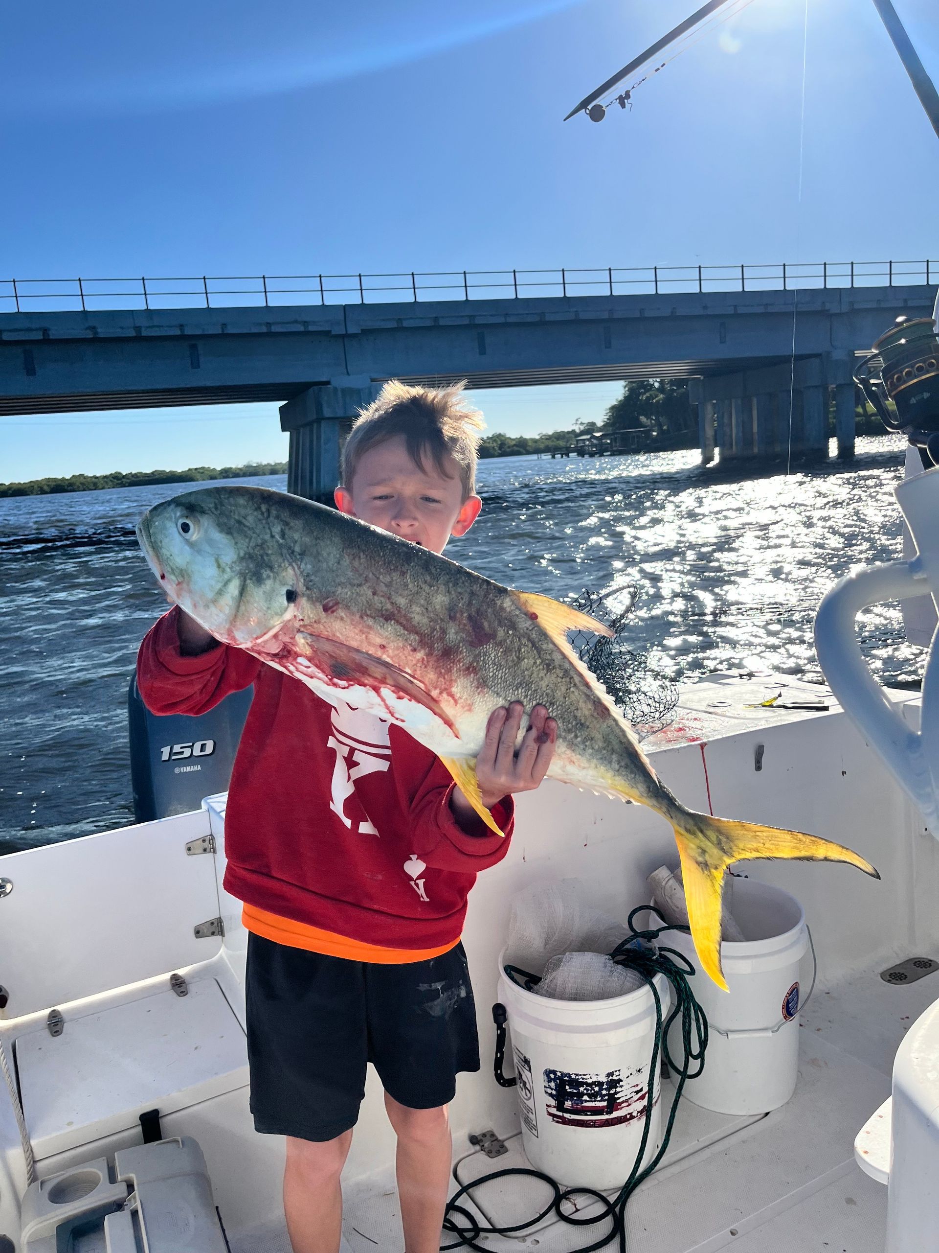 A young boy is holding a large fish on a boat