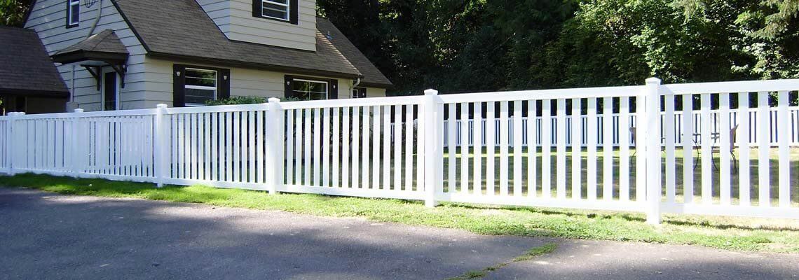 A white fence surrounds a house with a thatched roof