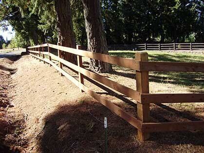 A wooden fence surrounds a dirt field with trees in the background