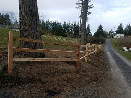 A wooden fence is sitting next to a tree on the side of a dirt road