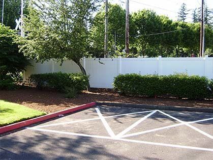 A parking lot with a white fence and trees in the background