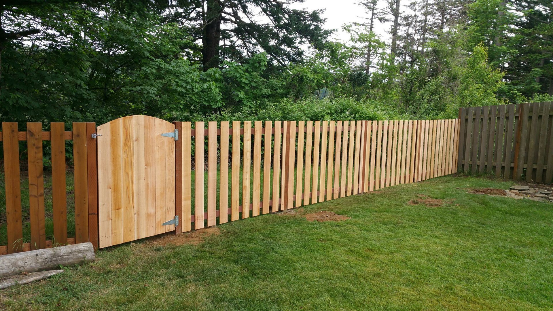 A wooden fence with a gate in the middle of a lush green yard