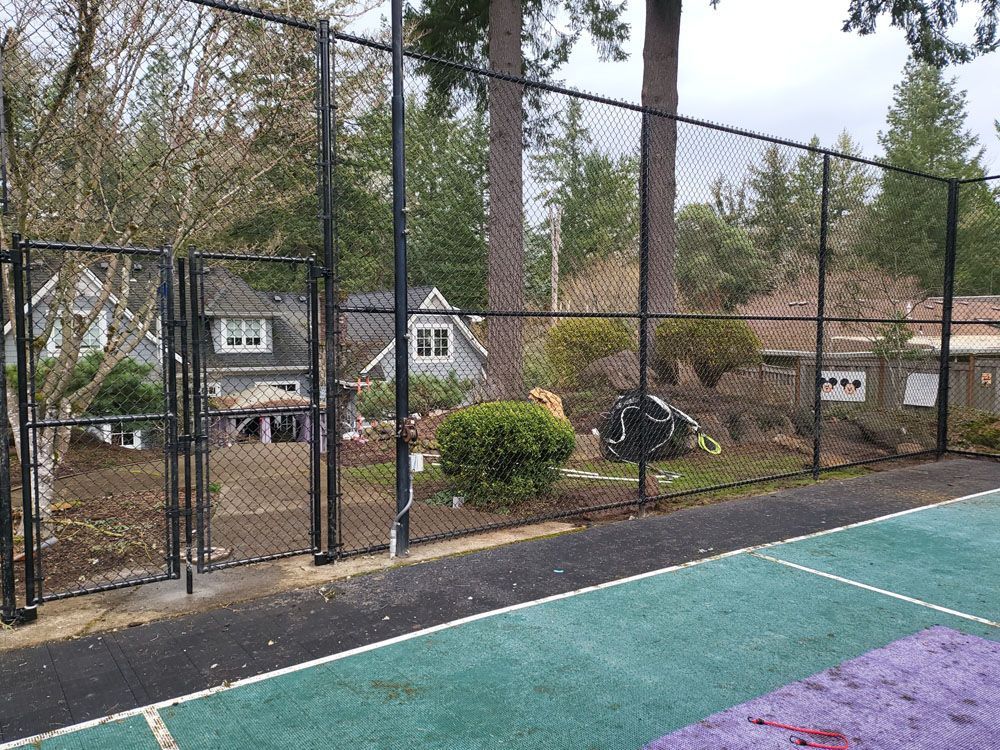 A tennis court with a chain link fence and a house in the background