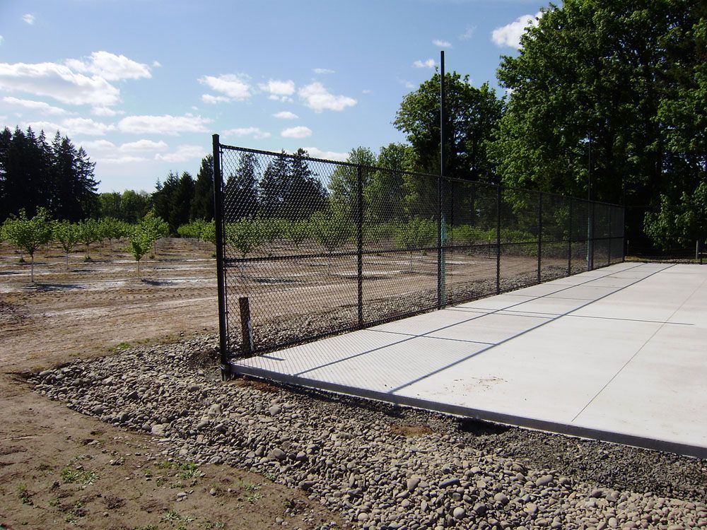 A chain link fence surrounds a concrete driveway with trees in the background