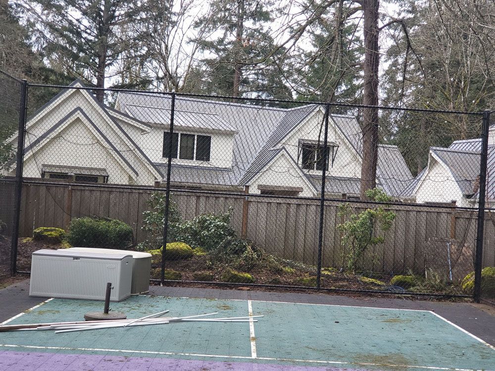 A tennis court in front of a house with a fence