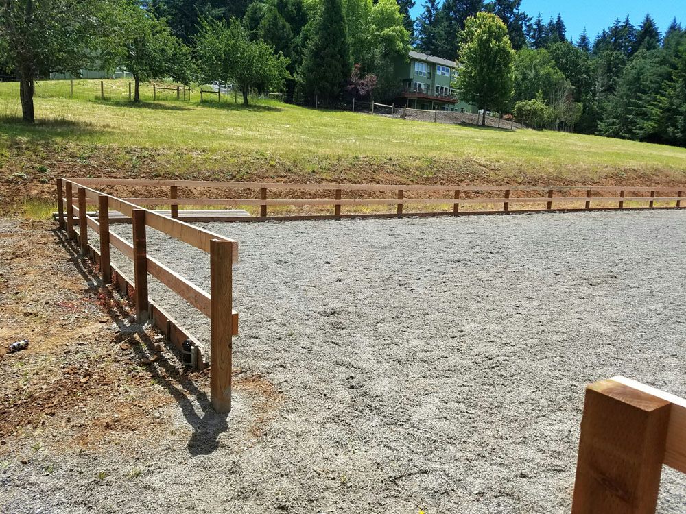 A wooden fence surrounds a dirt field with a house in the background