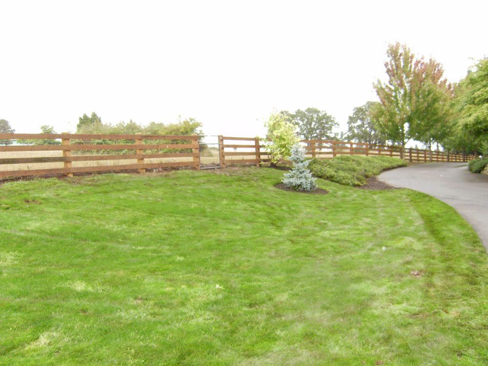 A wooden fence surrounds a large lush green field