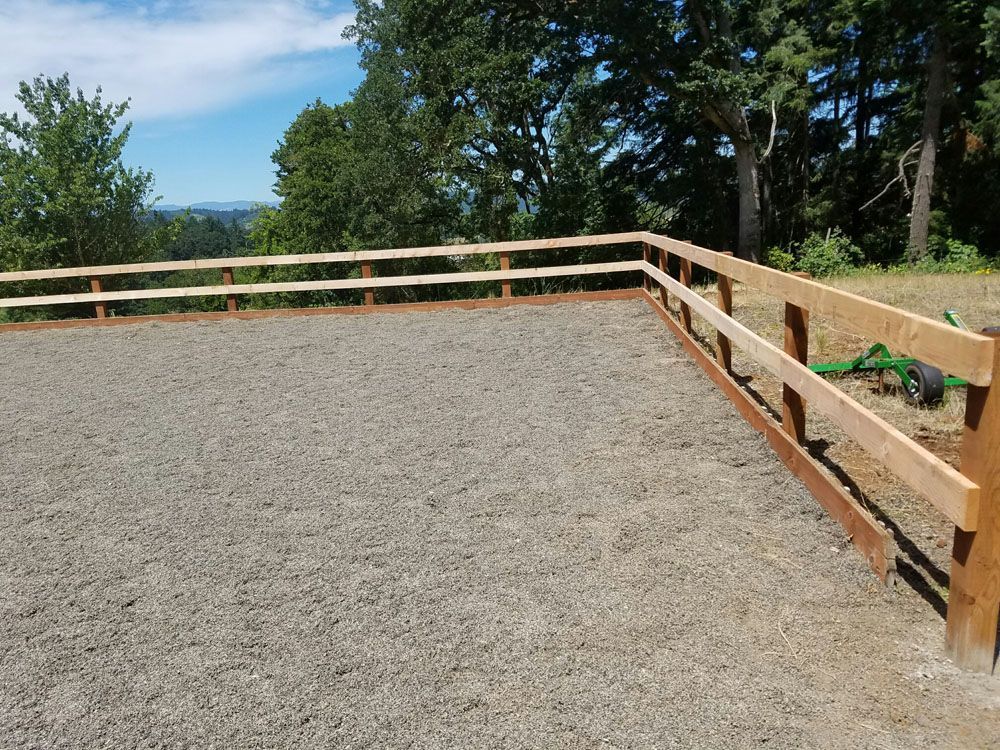A wooden fence surrounds a gravel area with trees