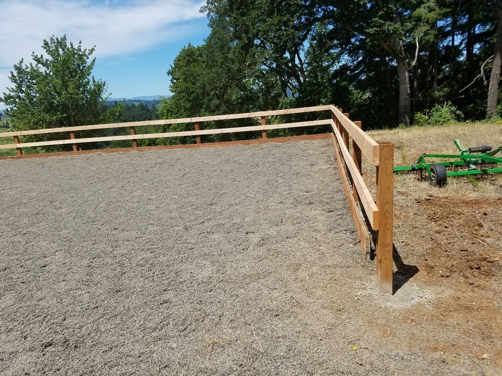 A wooden fence surrounds a gravel area with trees in the background