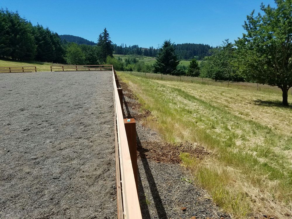 A wooden fence surrounds a dirt field with trees in the background