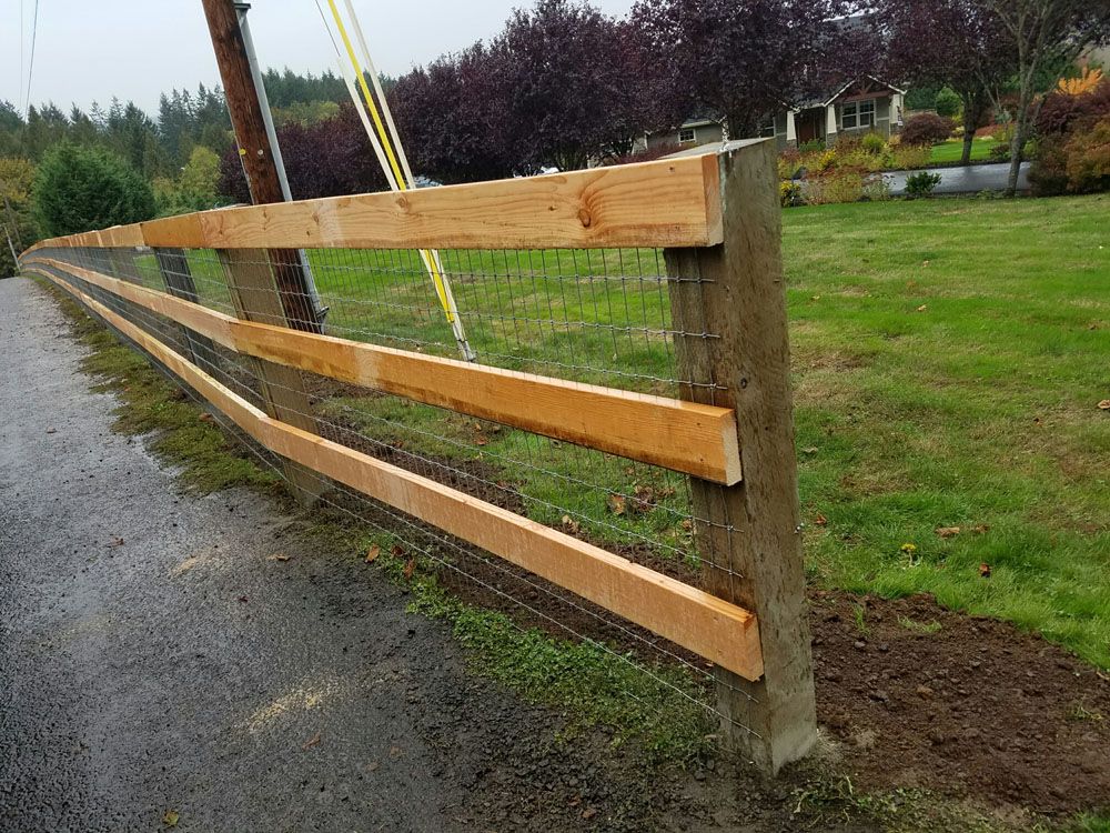 A wooden fence is sitting on the side of a road next to a grassy field