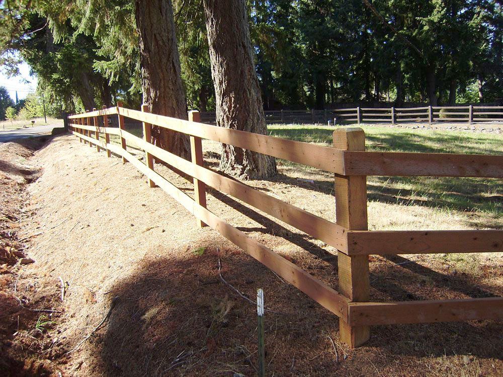 A wooden fence along a dirt road with trees in the background