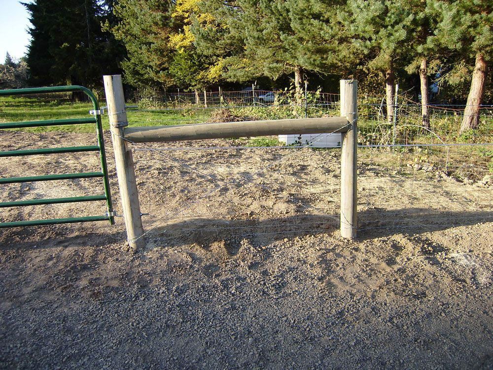 A wooden fence with a green gate in a dirt field