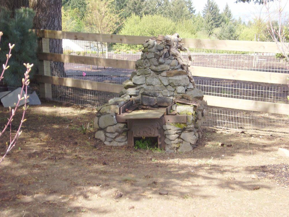 A wooden fence surrounds a stone fireplace in the dirt