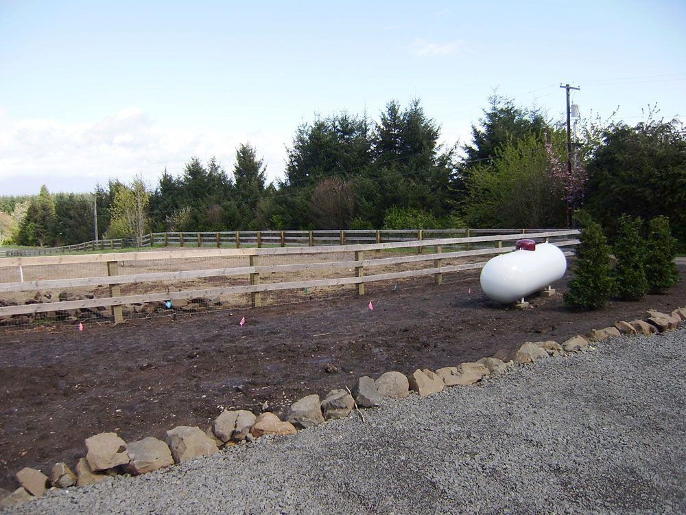 A white propane tank beside a wooden fence
