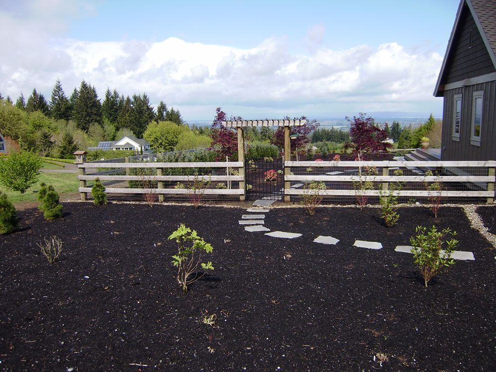 A fence surrounds a garden with a house in the background