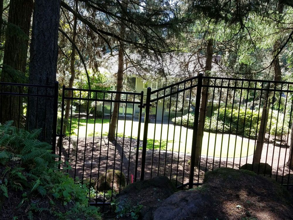 A black wrought iron fence surrounds a house in the woods