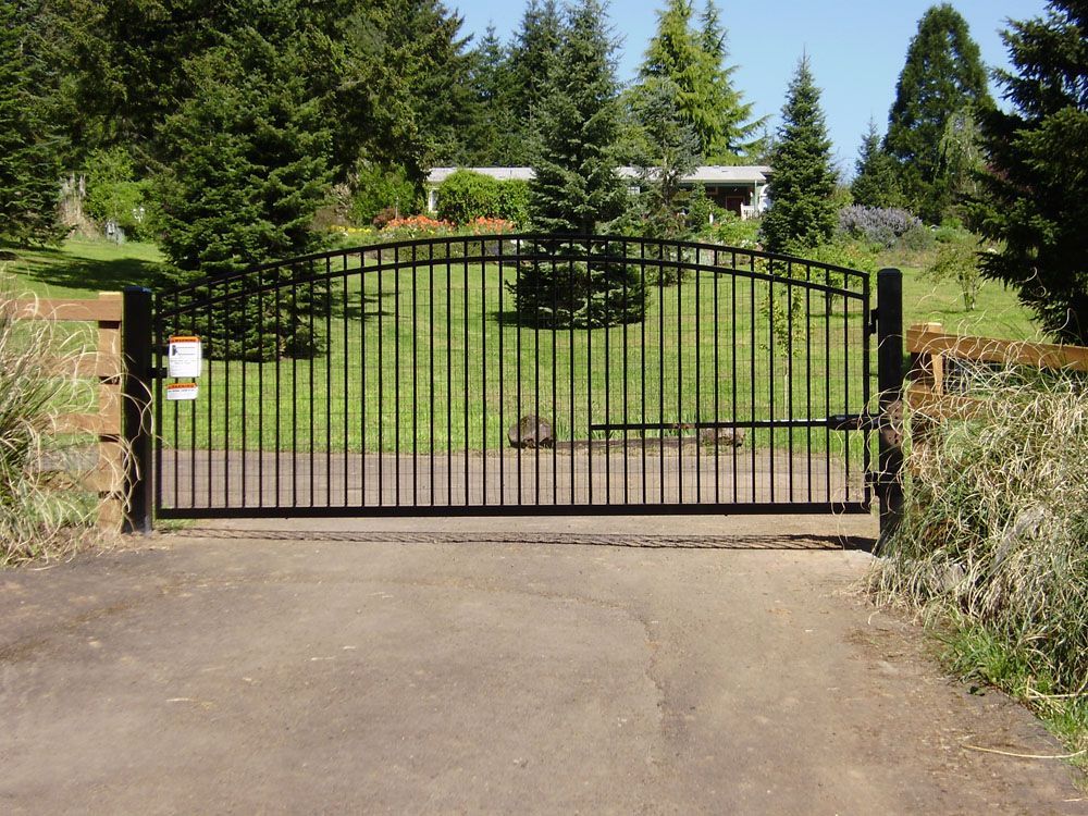 A black gate is open to a driveway with trees in the background