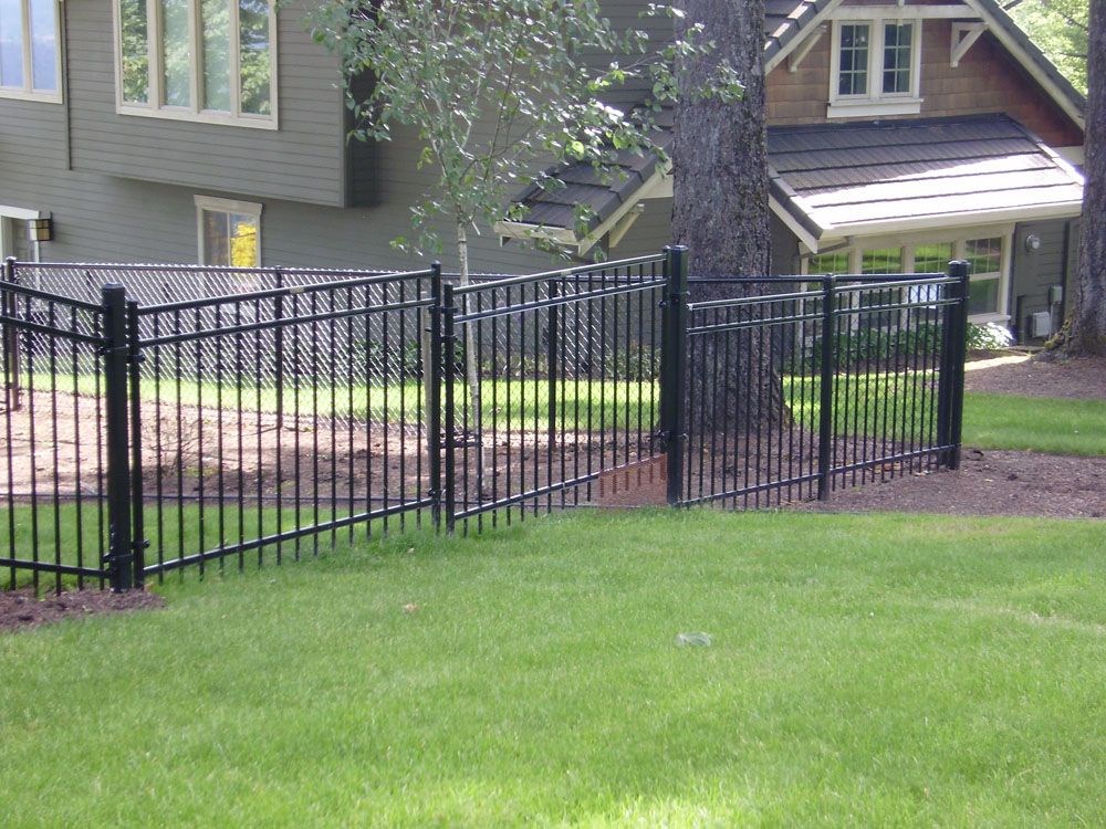 A black metal fence surrounds a lush green lawn in front of a house