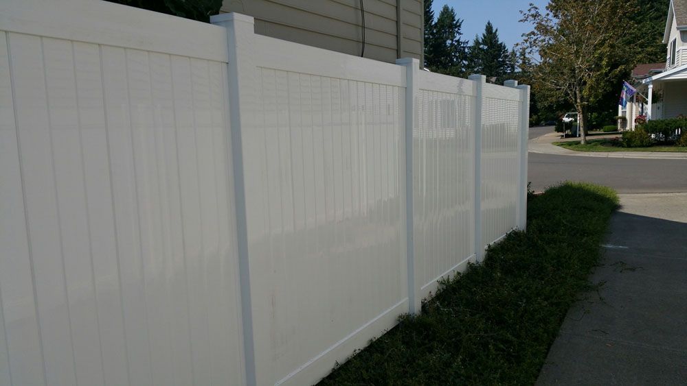 A white fence is sitting next to a sidewalk in front of a house