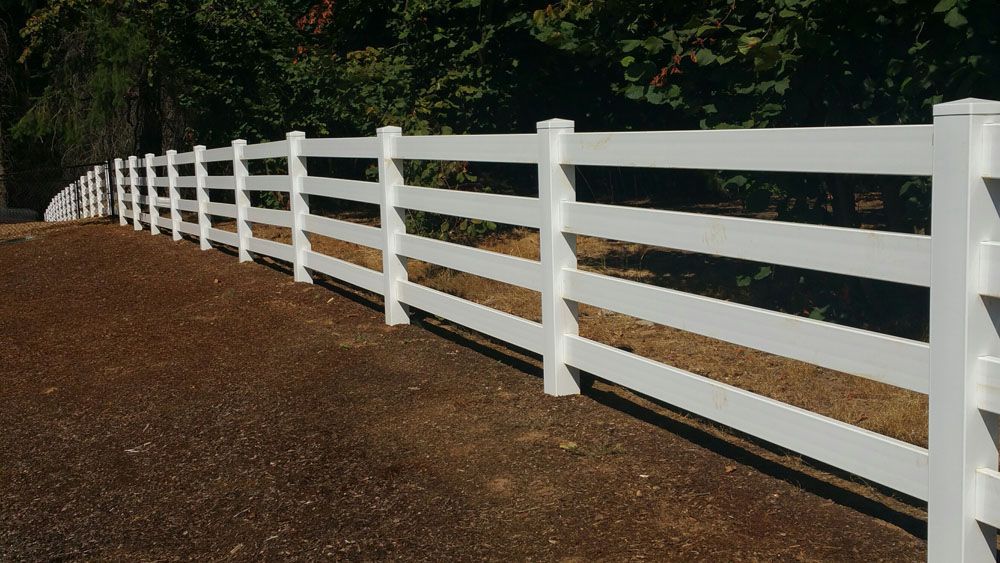 A white fence surrounds a dirt road with trees in the background