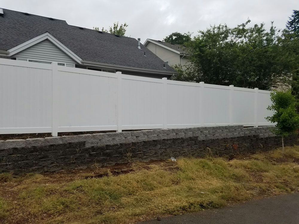 A white vinyl fence surrounds a stone wall in front of a house