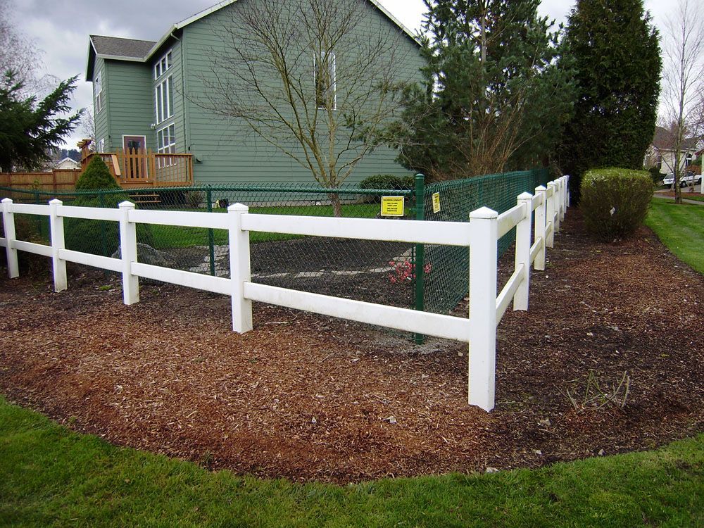 A white fence with a green chain link fence in front of a house