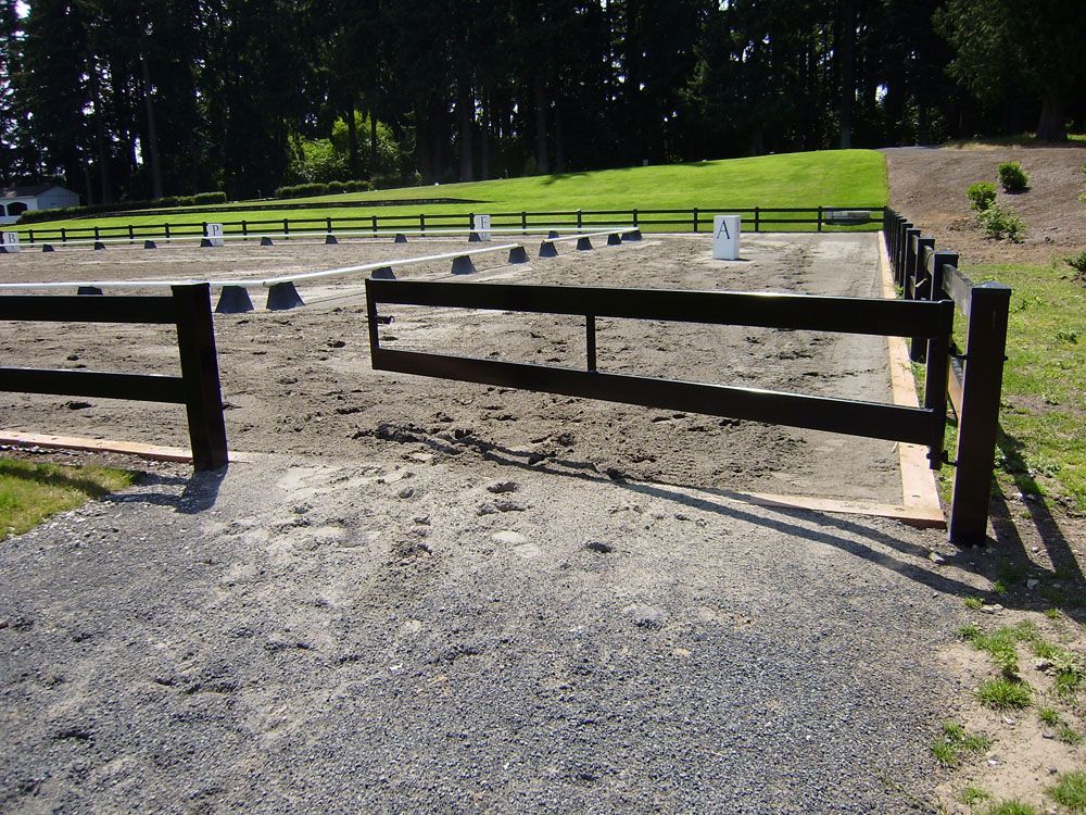 A vinly fence surrounds a dirt field with trees in the background