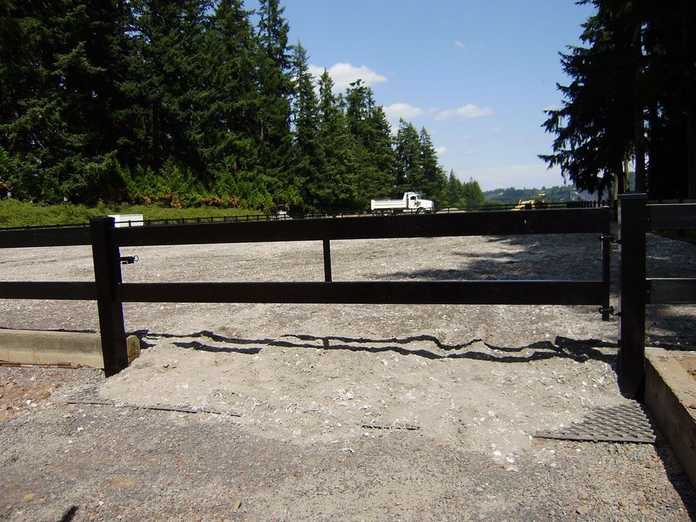 A black vinyl fence surrounds a gravel area with trees in the background