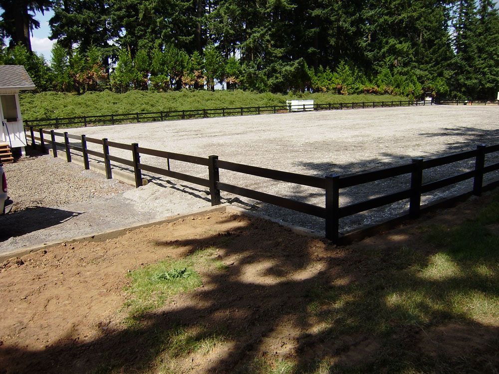 A fence surrounds a dirt field with trees in the background
