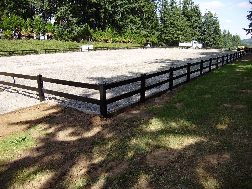 A wooden fence surrounds a dirt field with trees in the background
