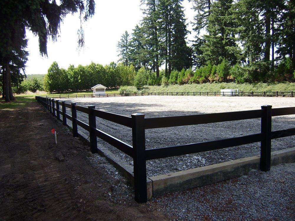 A black fence surrounds a gravel area with trees in the background