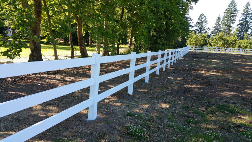 A vinyl fence surrounds a grassy field with trees in the background