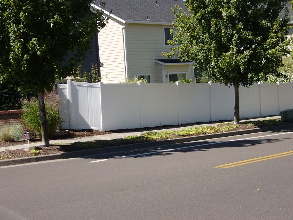 A white fence surrounds a house on the side of the road