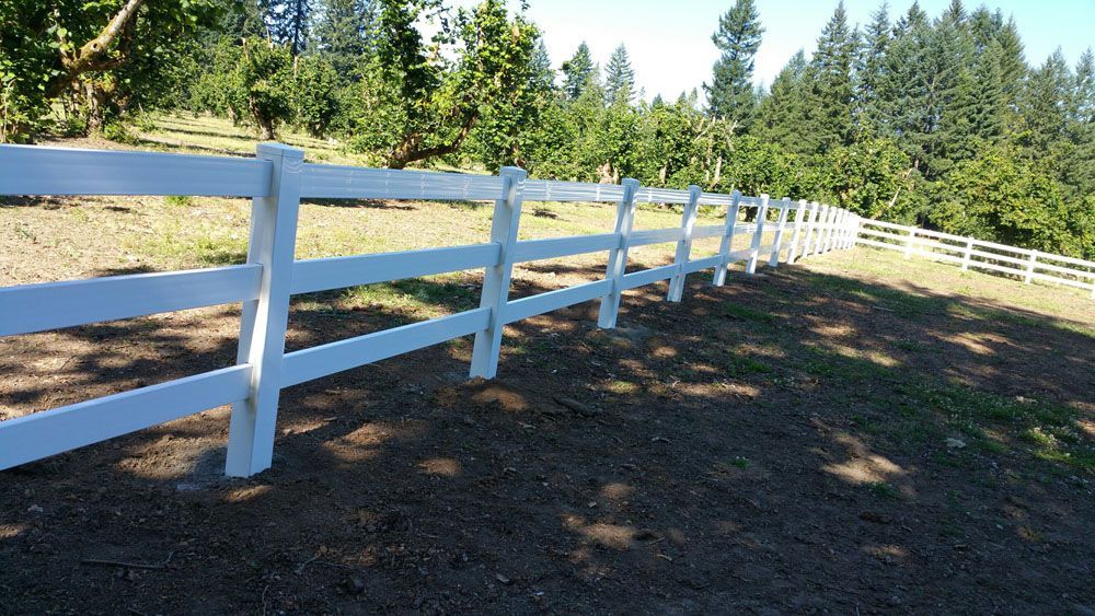 A white fence surrounds a field with trees in the background