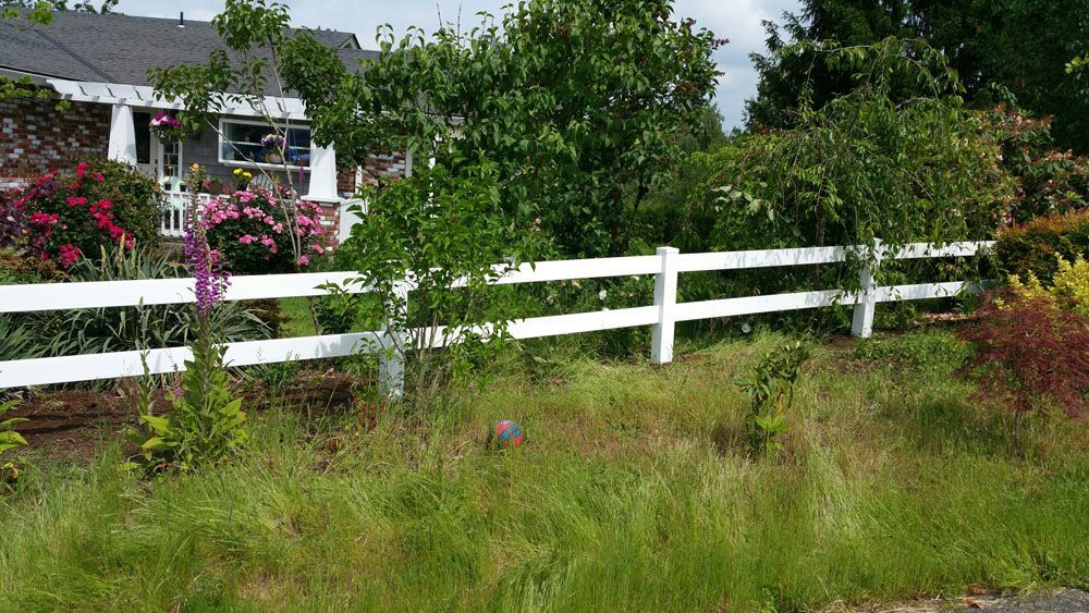 A white fence surrounds a lush green yard in front of a house