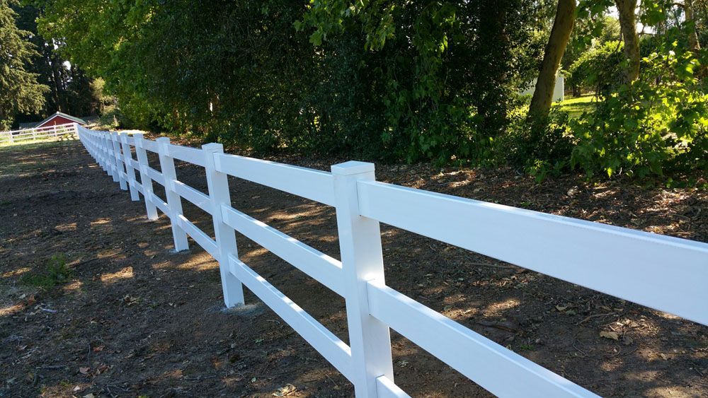 A white fence is surrounded by trees and dirt