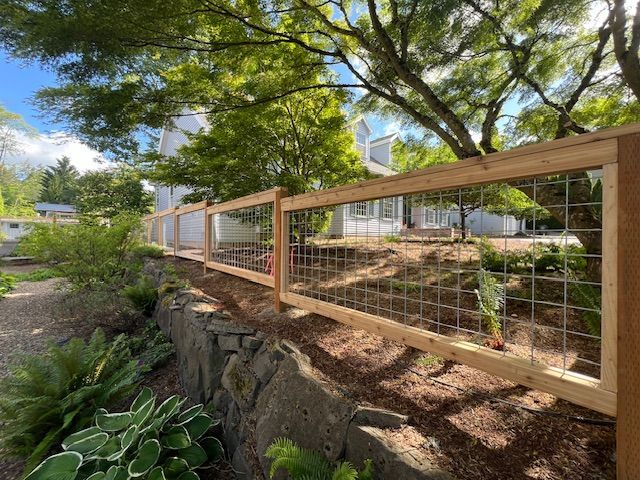 A wooden fence surrounds a stone wall in front of a house