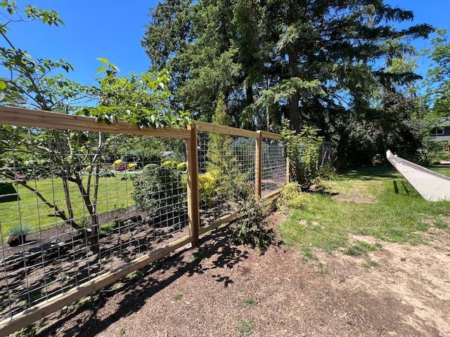 A wooden fence surrounds a yard with trees in the background