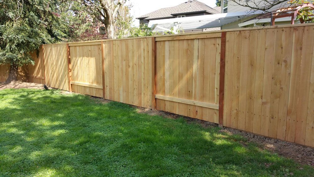 A wooden fence surrounds a lush green lawn in a backyard