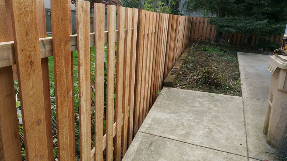 A wooden fence surrounds a concrete walkway in a backyard