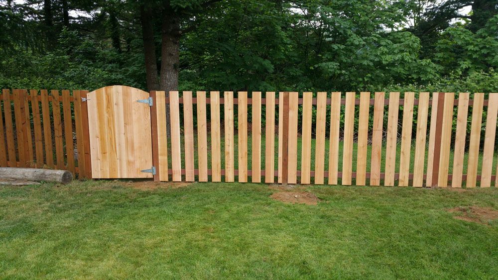 A wooden fence with a gate in the middle of a lush green field