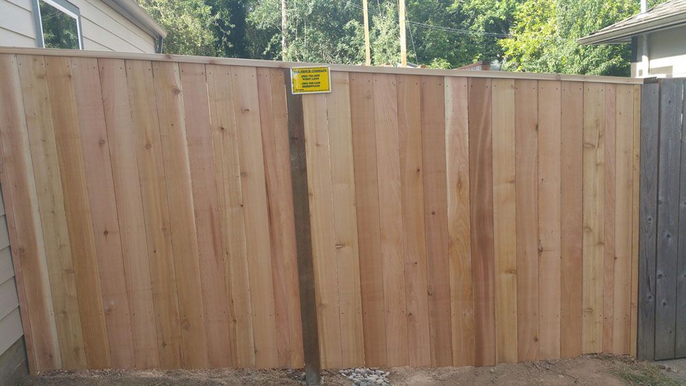 A wooden fence with a yellow sign on it in front of a house