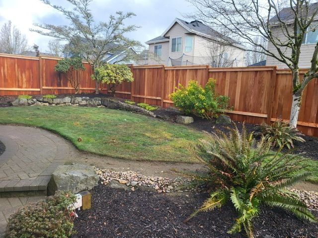 A backyard with a wooden fence and a house in the background