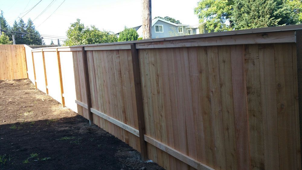 A wooden fence in a backyard with a house in the background