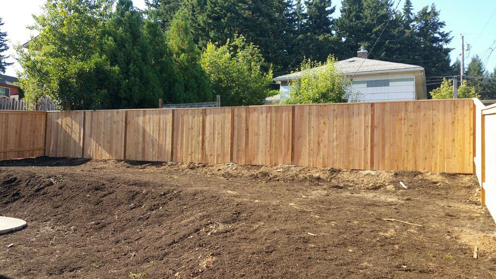 A wooden fence is surrounding a dirt field in a backyard