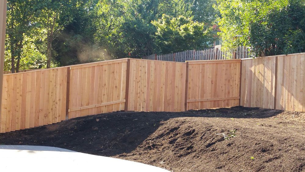 A wooden fence surrounds a pile of dirt in a backyard
