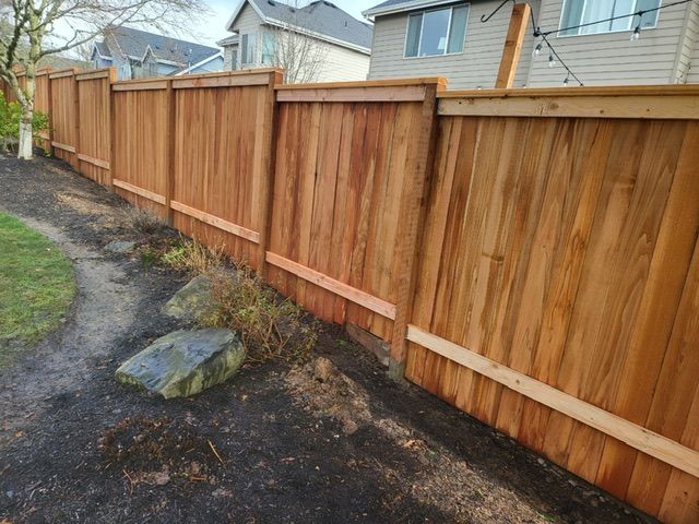 A wooden fence is sitting on the side of a dirt road next to a house