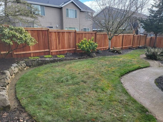 A wooden fence surrounds a lush green lawn in a backyard
